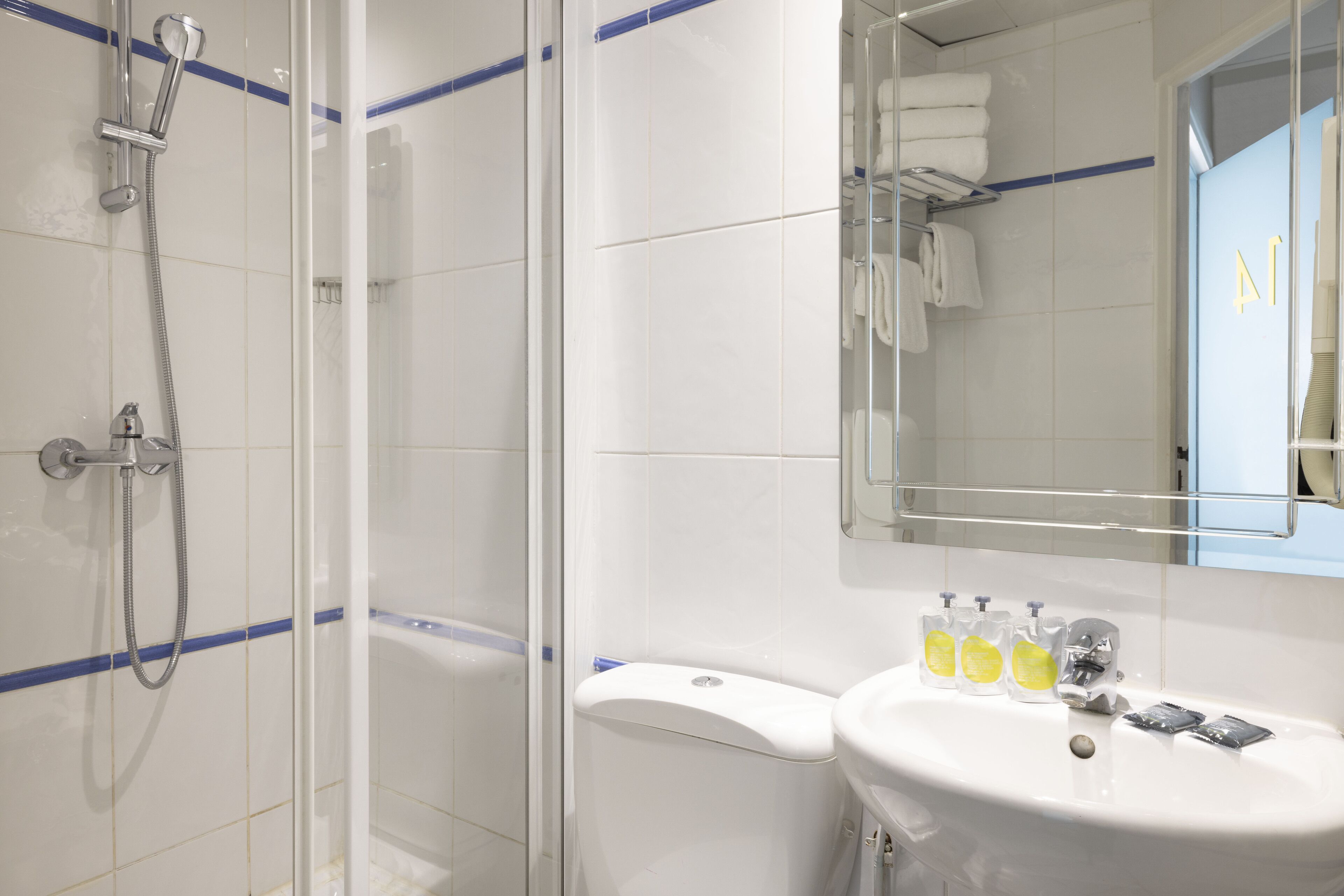 Een moderne badkamer met een douchecabine van glas, een wit wastafelmeubel met zeepdispensers en een spiegel erboven.