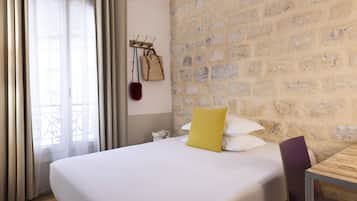 Una habitación de hotel con una cama, una mesa de madera, una pared de piedra y una ventana con cortinas.