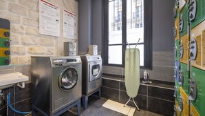 A laundry room with two front-loading washing machines, a drying machine, and a rack of dryers.