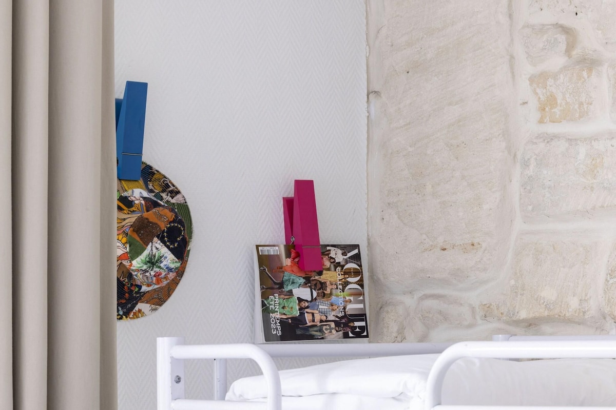 Una habitación con una cama blanca, una pared con textura y una revista sobre un atril.