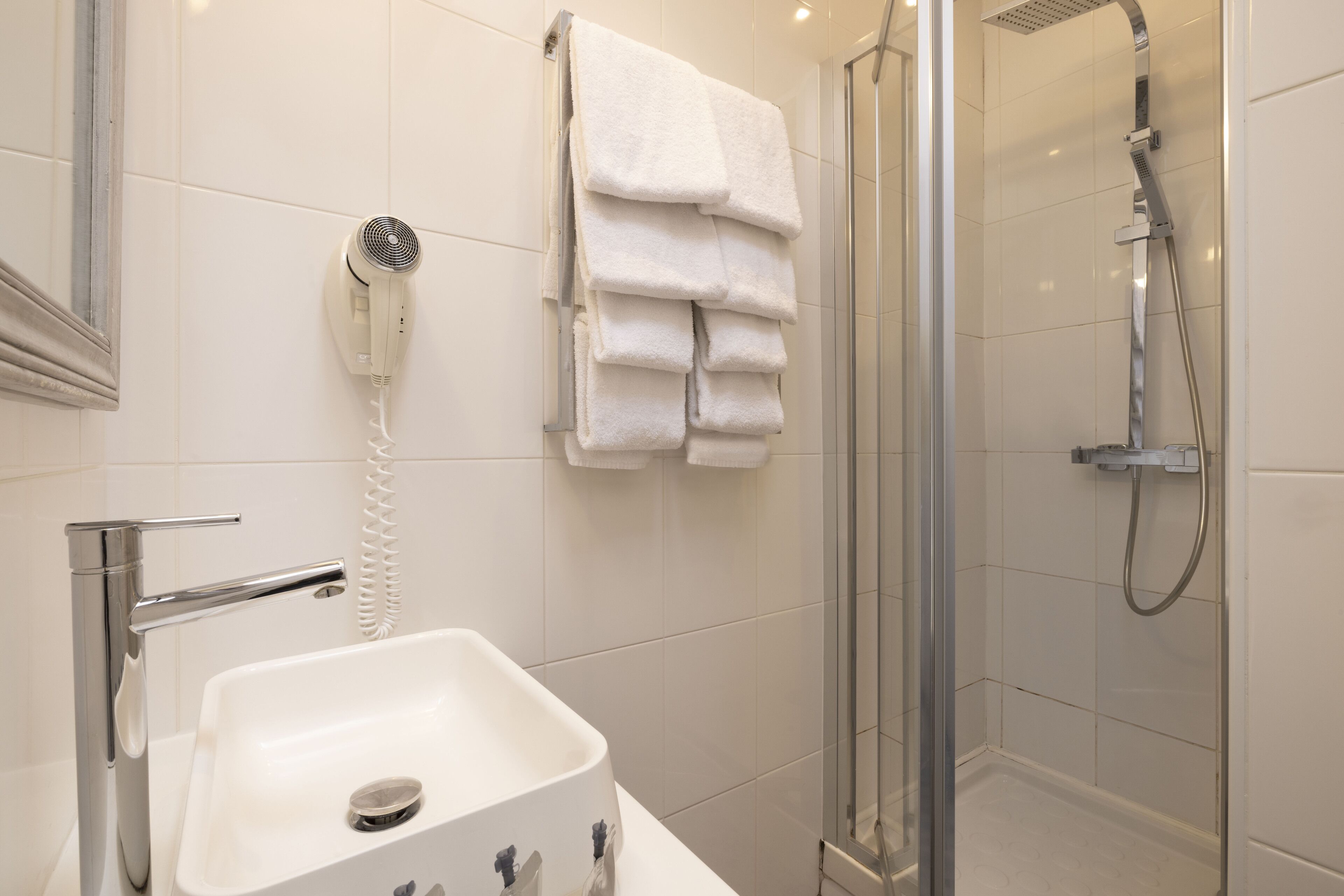 A modern bathroom with a glass-enclosed shower, a white sink, and a hairdryer mounted on the wall.