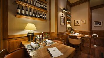 Un comedor con una mesa de madera dispuesta para dos, una estantería para vinos arriba y cuadros en la pared.