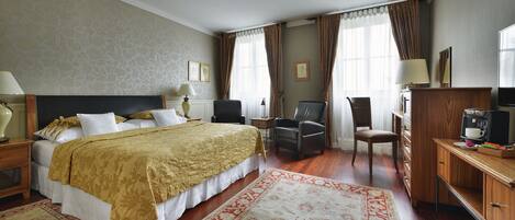A hotel room with a large bed, two chairs, a desk with a coffee maker, and a TV.