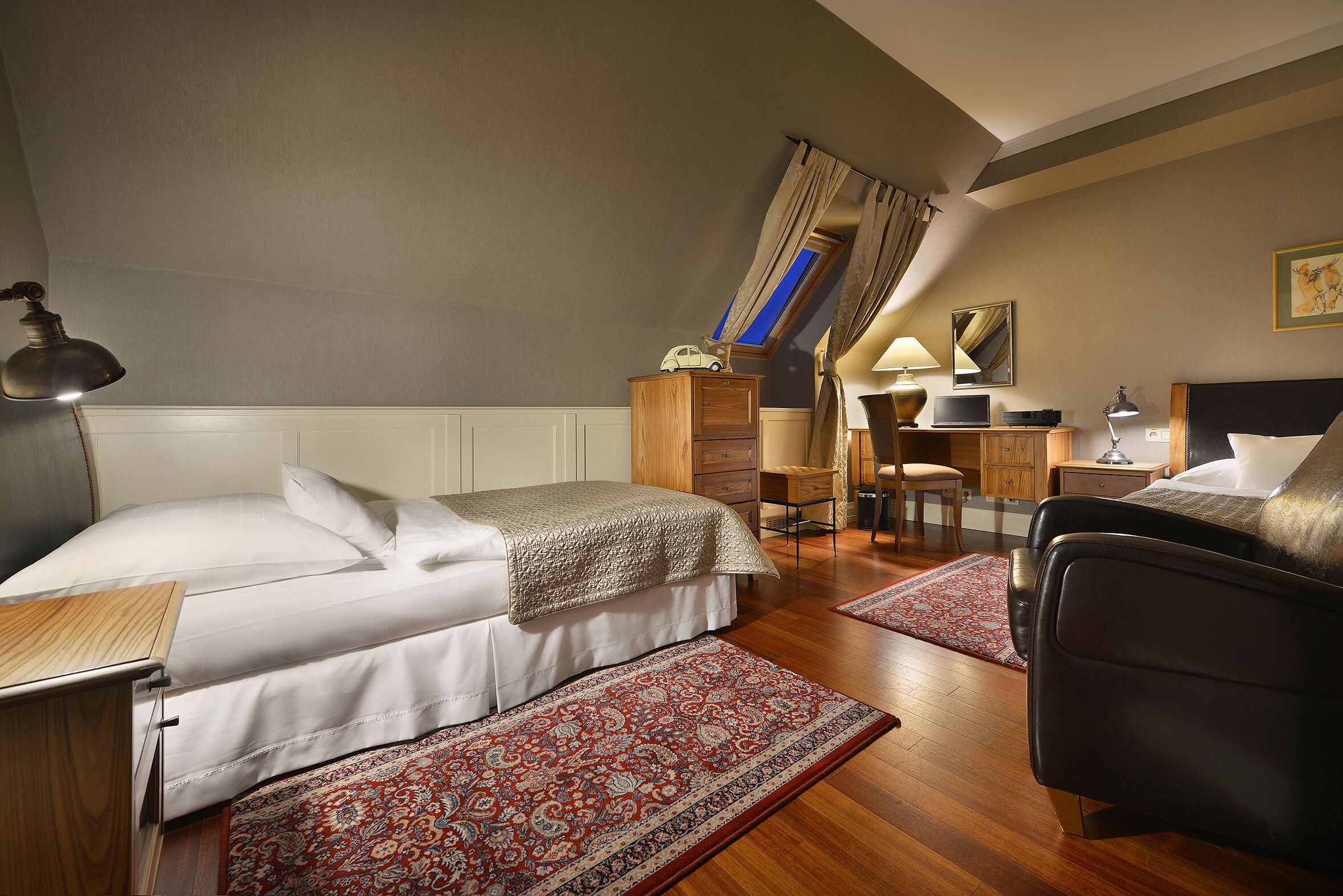 Ein Hotelzimmer mit zwei Betten, einem Schreibtisch, einem Stuhl, einer Lampe und einem gemusterten Teppich.