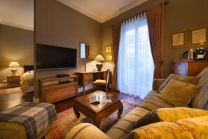 A living room with a television, wooden furniture, a coffee maker, and a window with curtains. - Marrol's Boutique Hotel (Bratislava)