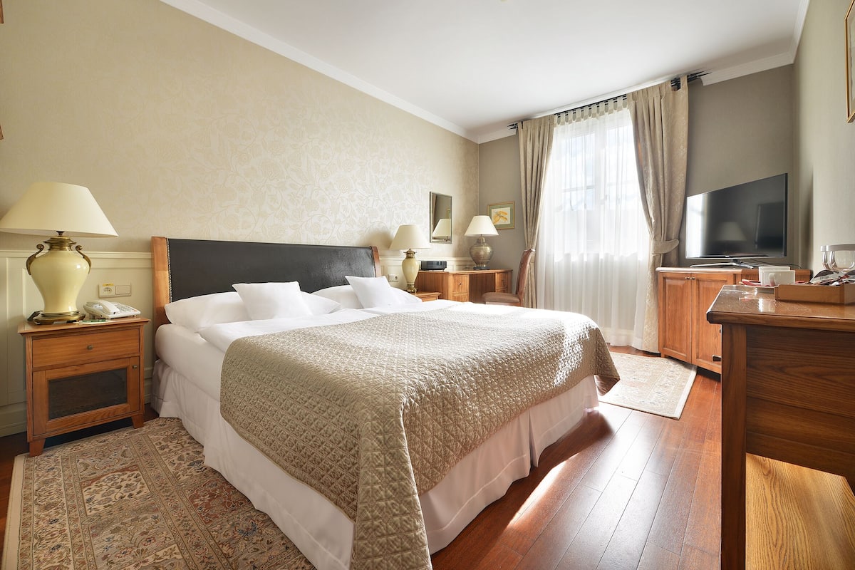 Een hotelkamer met een groot bed, een televisie, een houten nachtkastje, een bureau en een bureaulamp.