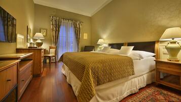 A hotel room with a large bed, two bedside tables with lamps, a desk, a chair, and a window with curtains.