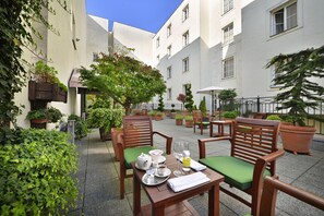 An outdoor patio area with wooden chairs and tables, potted plants, and a clear blue sky. - Marrol's Boutique Hotel (Bratislava)