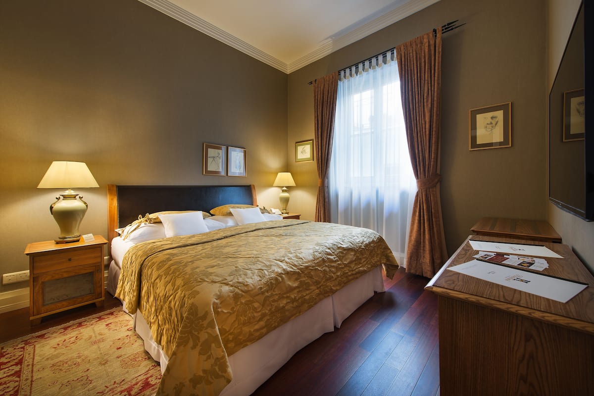 Een hotelkamer met een groot bed, twee nachtkastjes met lampen, een houten bureau en een raam met gordijnen.