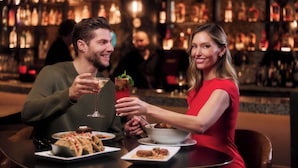 Una pareja cenando en un bar con varias botellas al fondo.