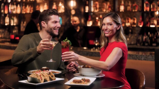Una pareja cenando en un bar con varias botellas al fondo.