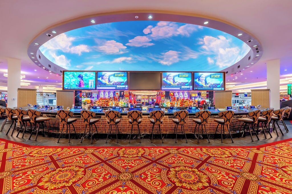 Un bar da casinò con schermi multipli, un grande affresco al soffitto e una moquette decorata.