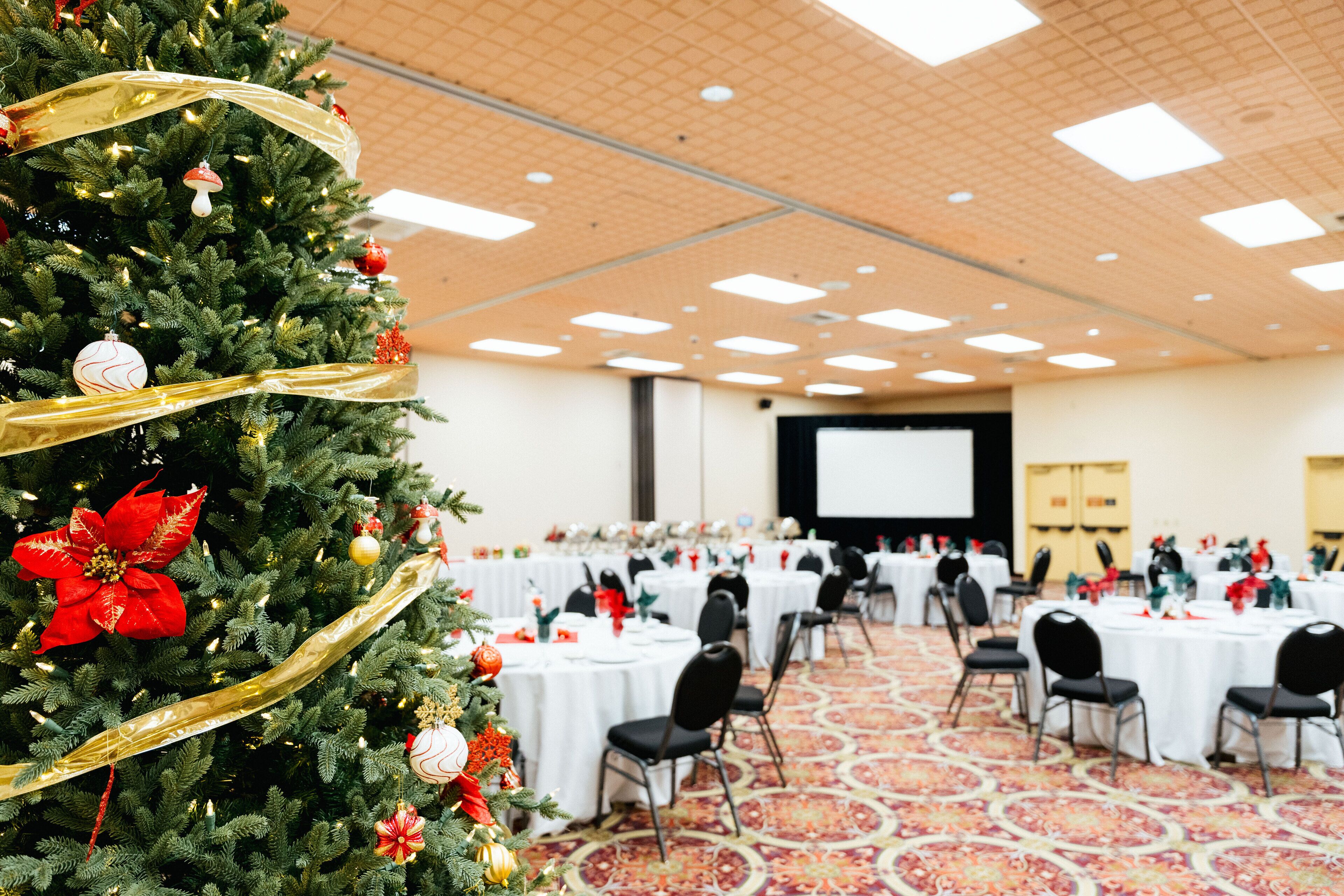 A conference room with round tables, black chairs, and a large Christmas tree with ornaments.