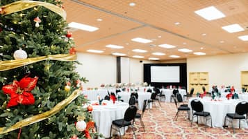 A conference room with round tables, black chairs, and a large Christmas tree with ornaments.
