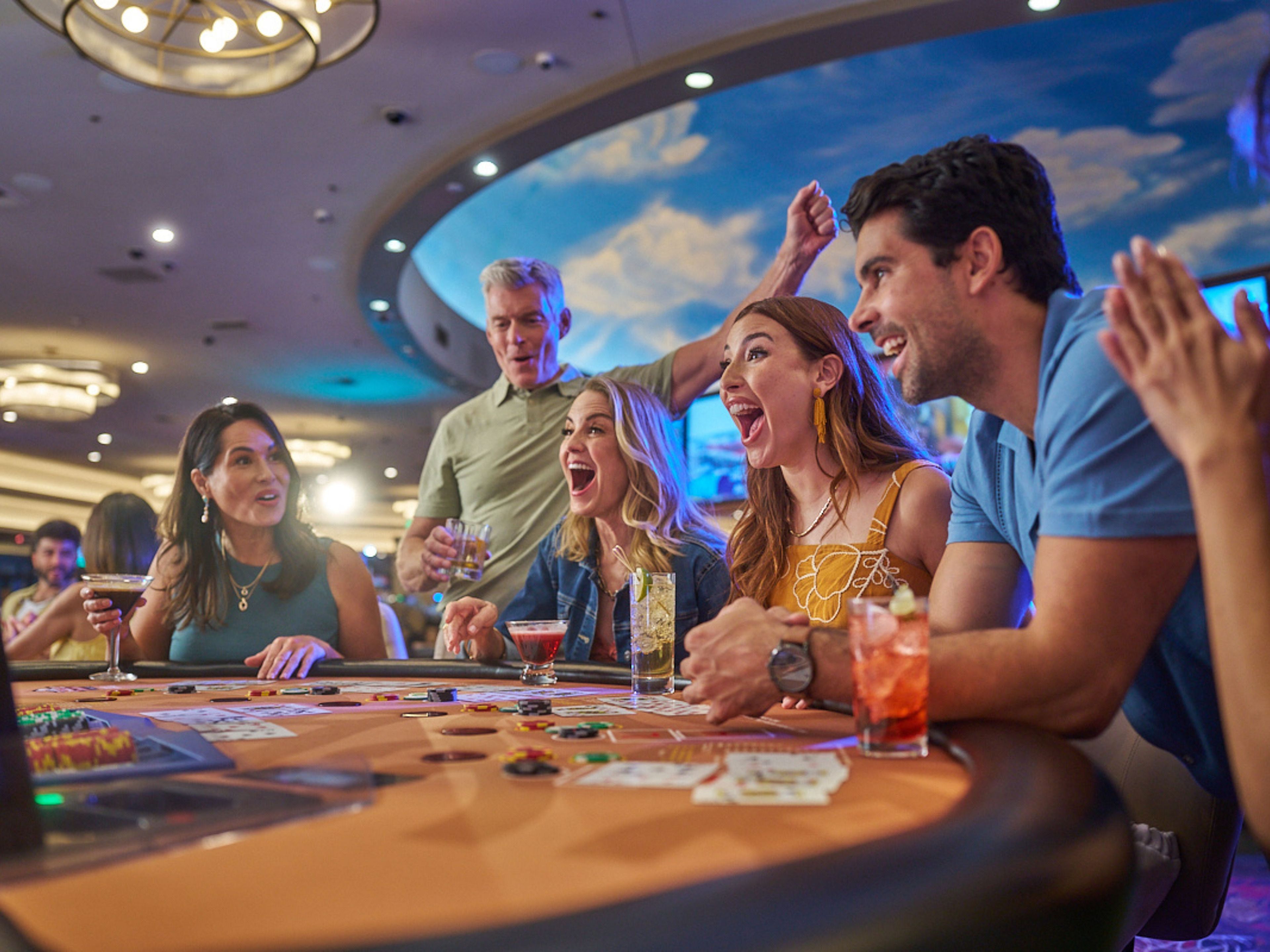 A group of people seated at a casino table with cards and chips, indicating a gambling activity.