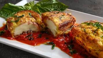 Een bord met gegrilde kipfilet gevuld met vulling, overgoten met rode saus en afgeleid met basilicum.