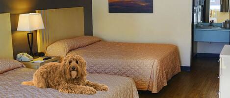 A hotel room with two beds, a painting of a sunset, a lamp, and a wooden floor.