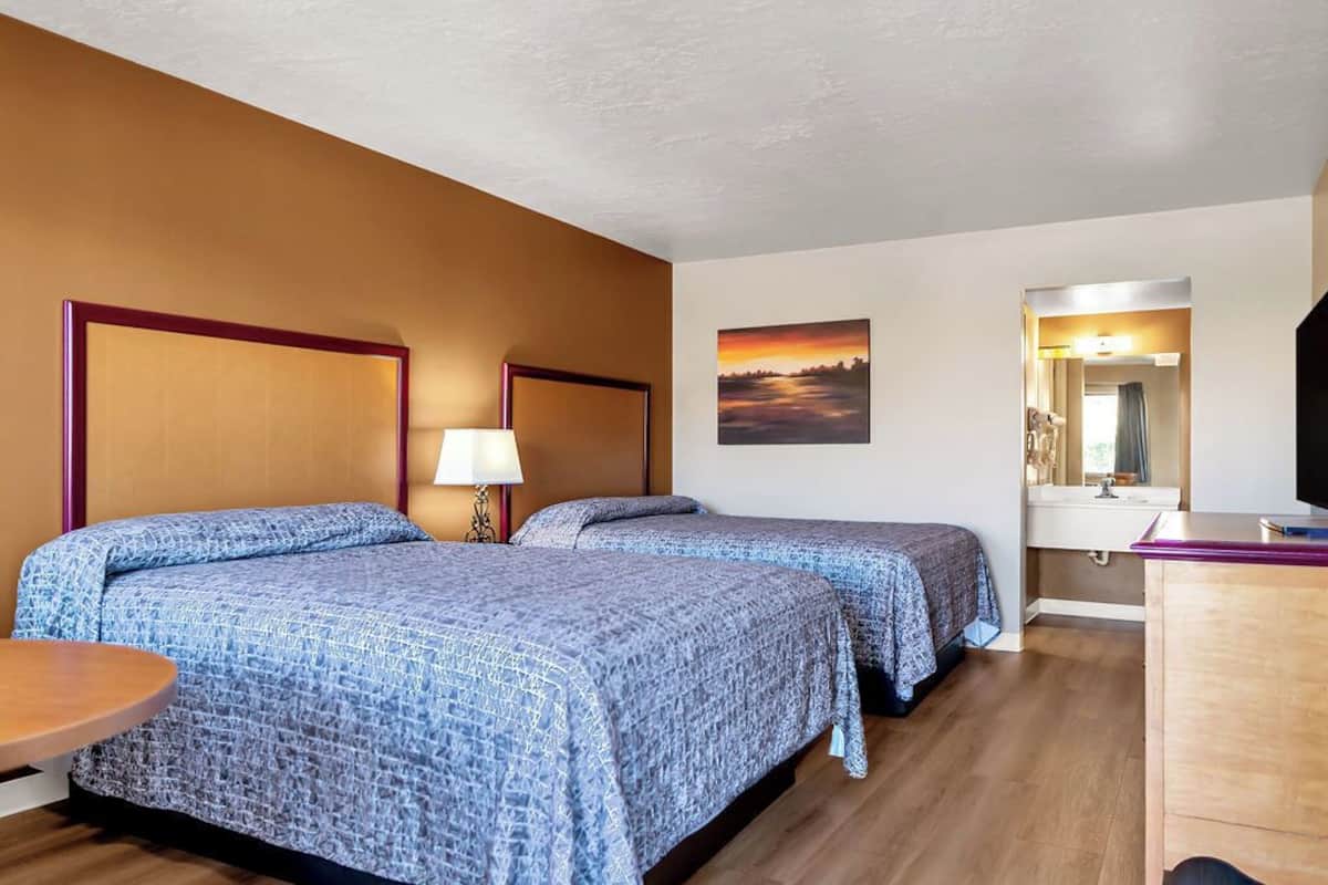 Une chambre d’hôtel avec deux lits, un bureau, une chaise, une lampe, un tableau et un miroir.