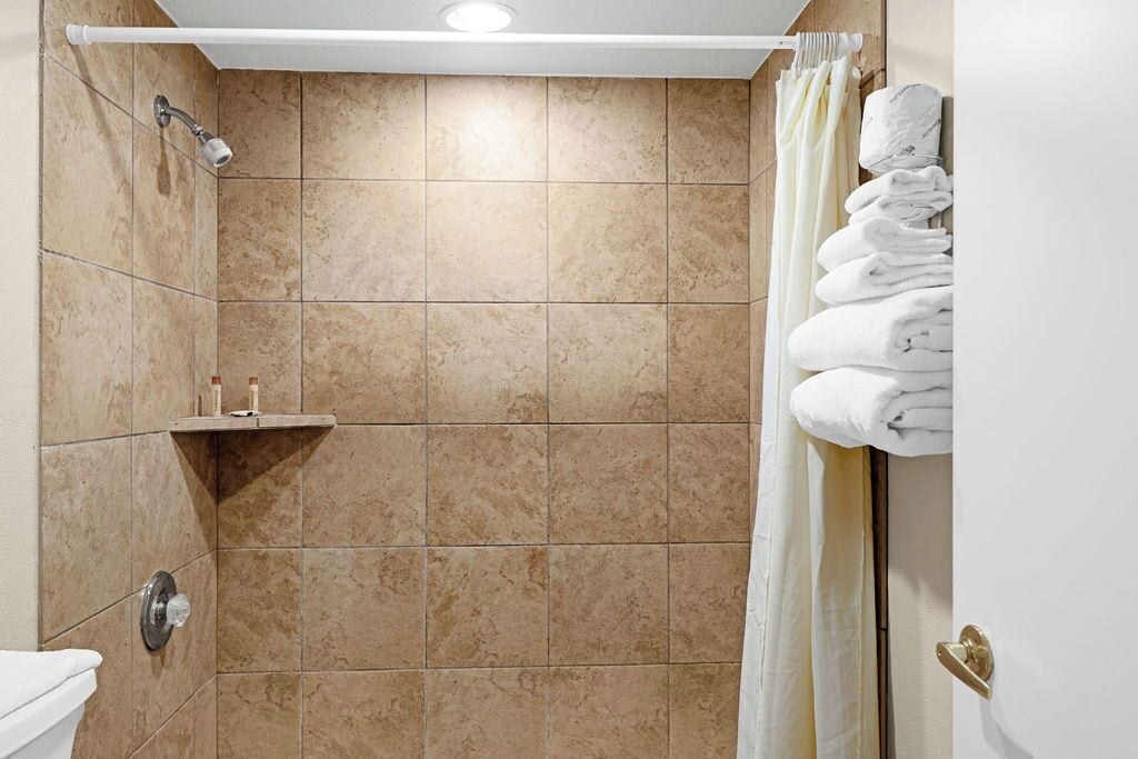 Un bagno con piastrelle color beige, una doccia, un WC e un portasacchiuni con asciugamani piegati.
