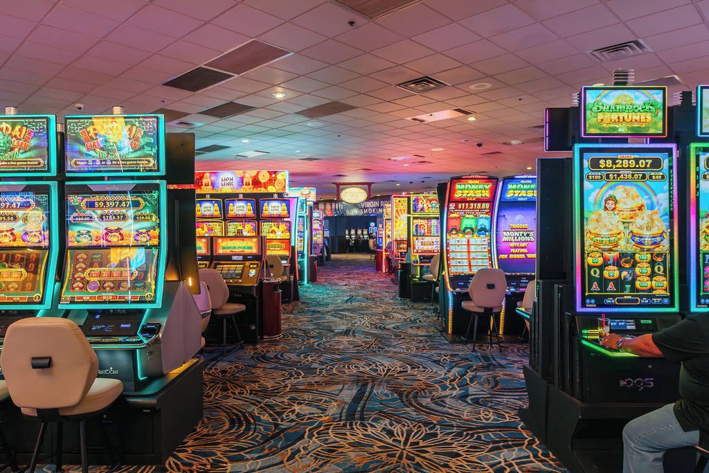 A casino floor with multiple slot machines and a carpeted floor.