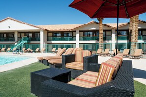 A poolside area with wicker furniture and a red umbrella.