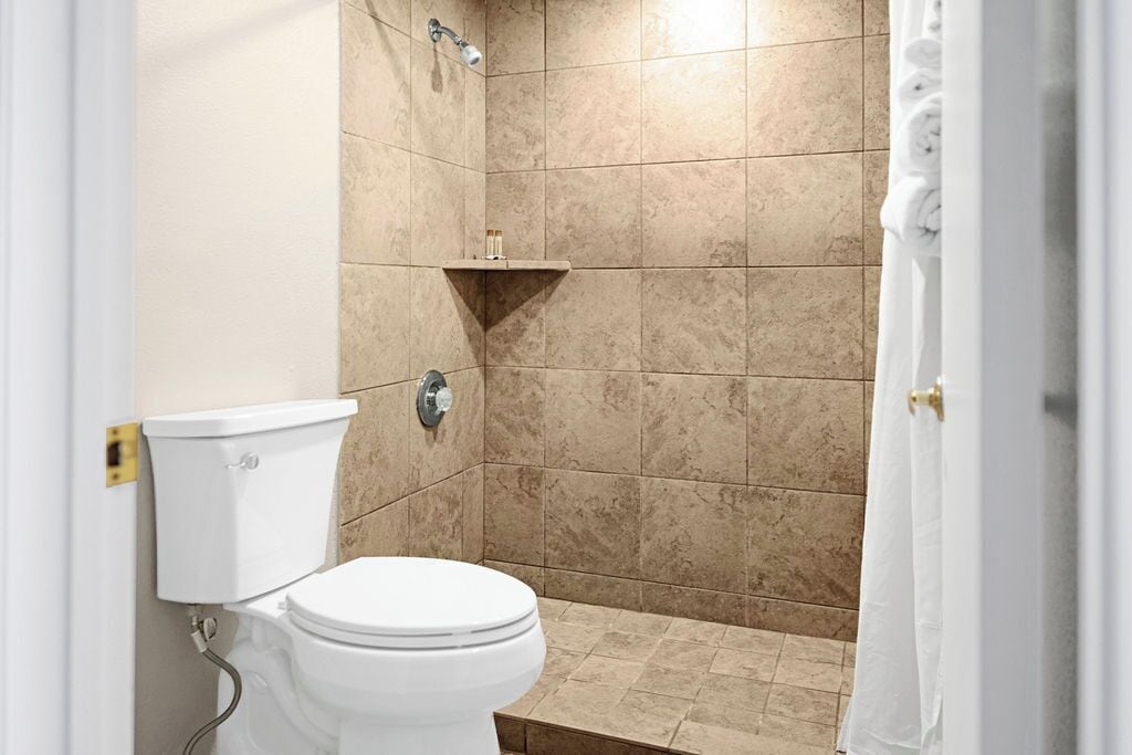 A small bathroom with a toilet, a shower, and a shelf with toiletries.