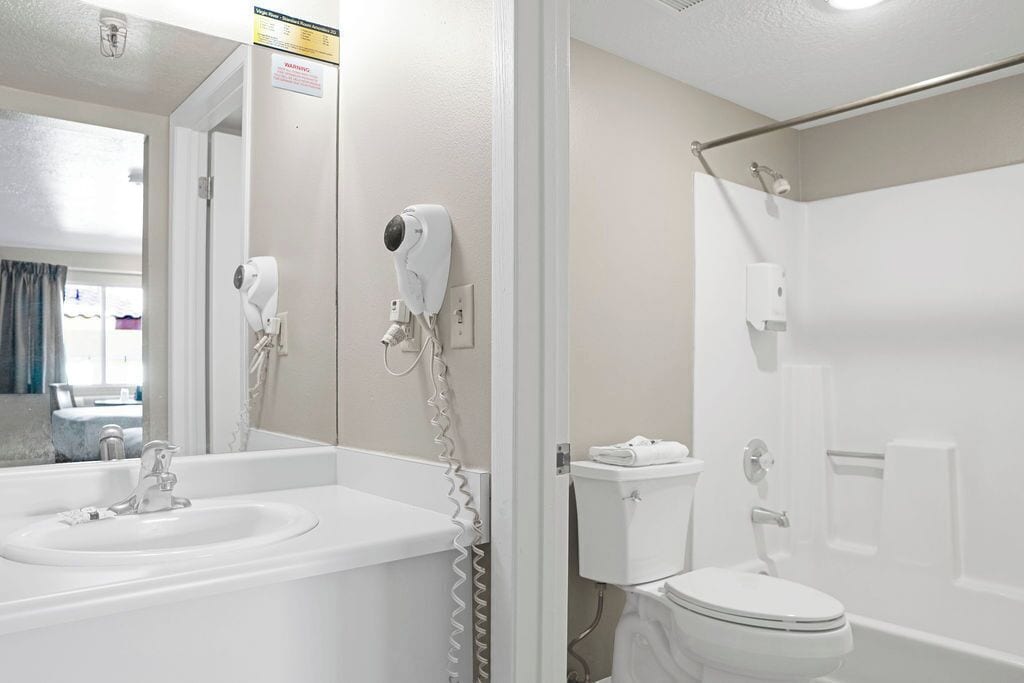 A bathroom with a sink, toilet, and shower. There is a hairdryer mounted on the wall.
