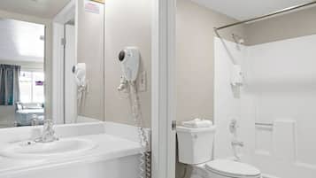 A bathroom with a sink, toilet, and shower. There is a hairdryer mounted on the wall.