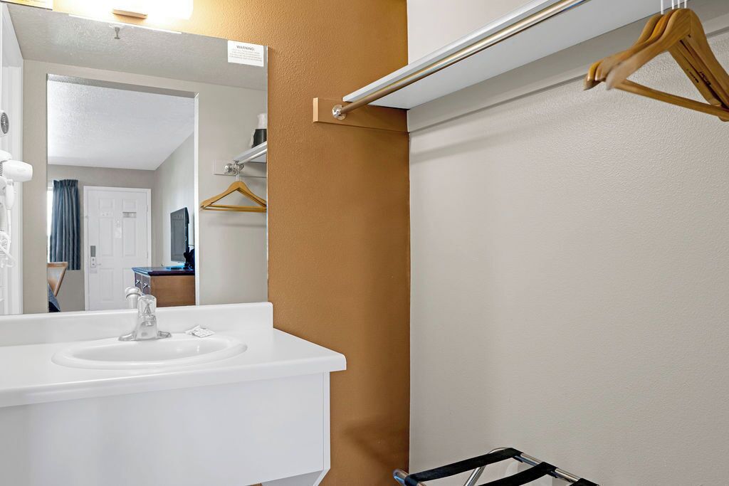 Un baño con un lavamanos blanco, un espejo y un perchero para toallas.