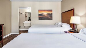 Ein Hotelzimmer mit zwei Betten, einem Sonnenuntergangsdruck, einer Nachttischlampe und einem kleinen Schreibtisch mit Telefon.