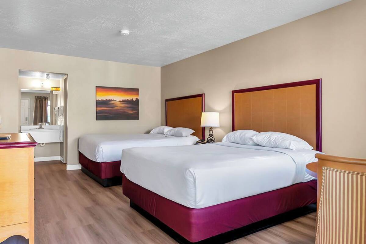 Une chambre d’hôtel avec deux lits, un bureau, un miroir et un tableau au mur.