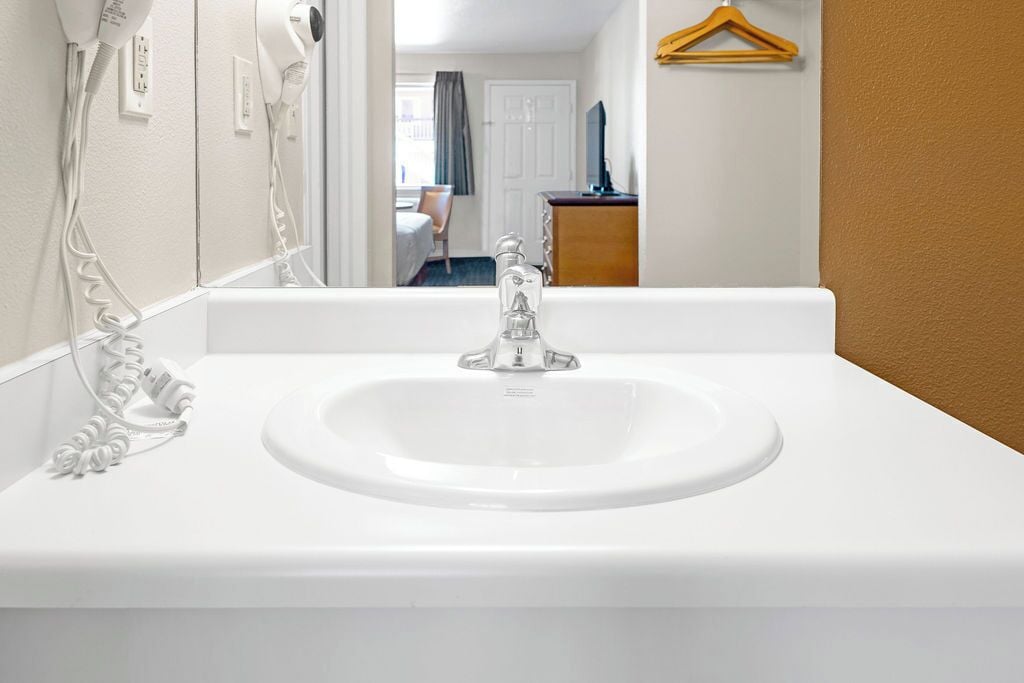A white bathroom sink with a mirror above it, a hairdryer on the wall, and a wooden hanger on the wall.