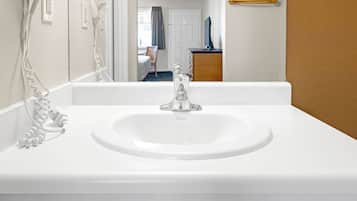 A white bathroom sink with a mirror above it, a hairdryer on the wall, and a wooden hanger on the wall.