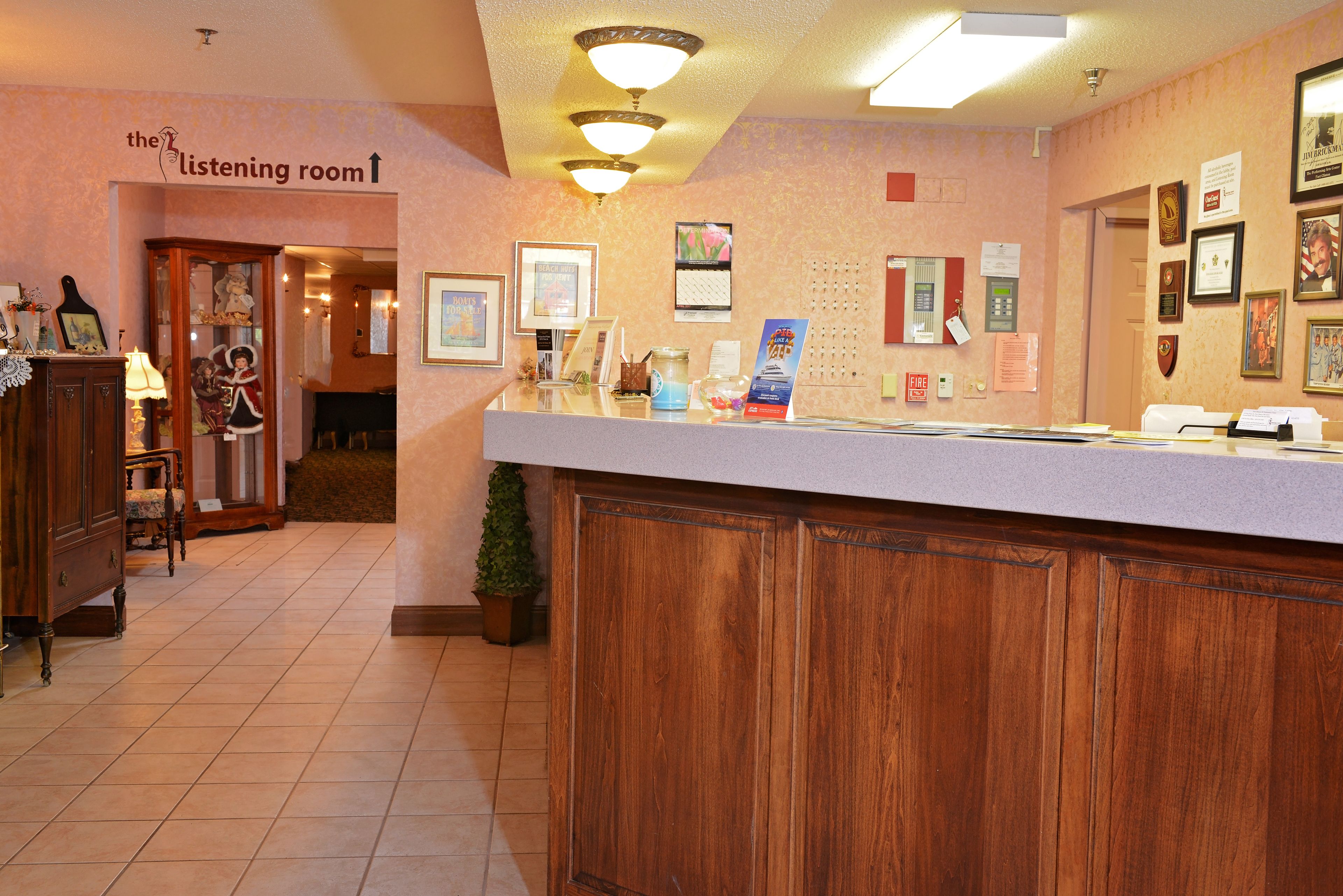 A reception area with a wooden counter, a sign for the listening room, framed pictures on the wall, and a small potted plant.