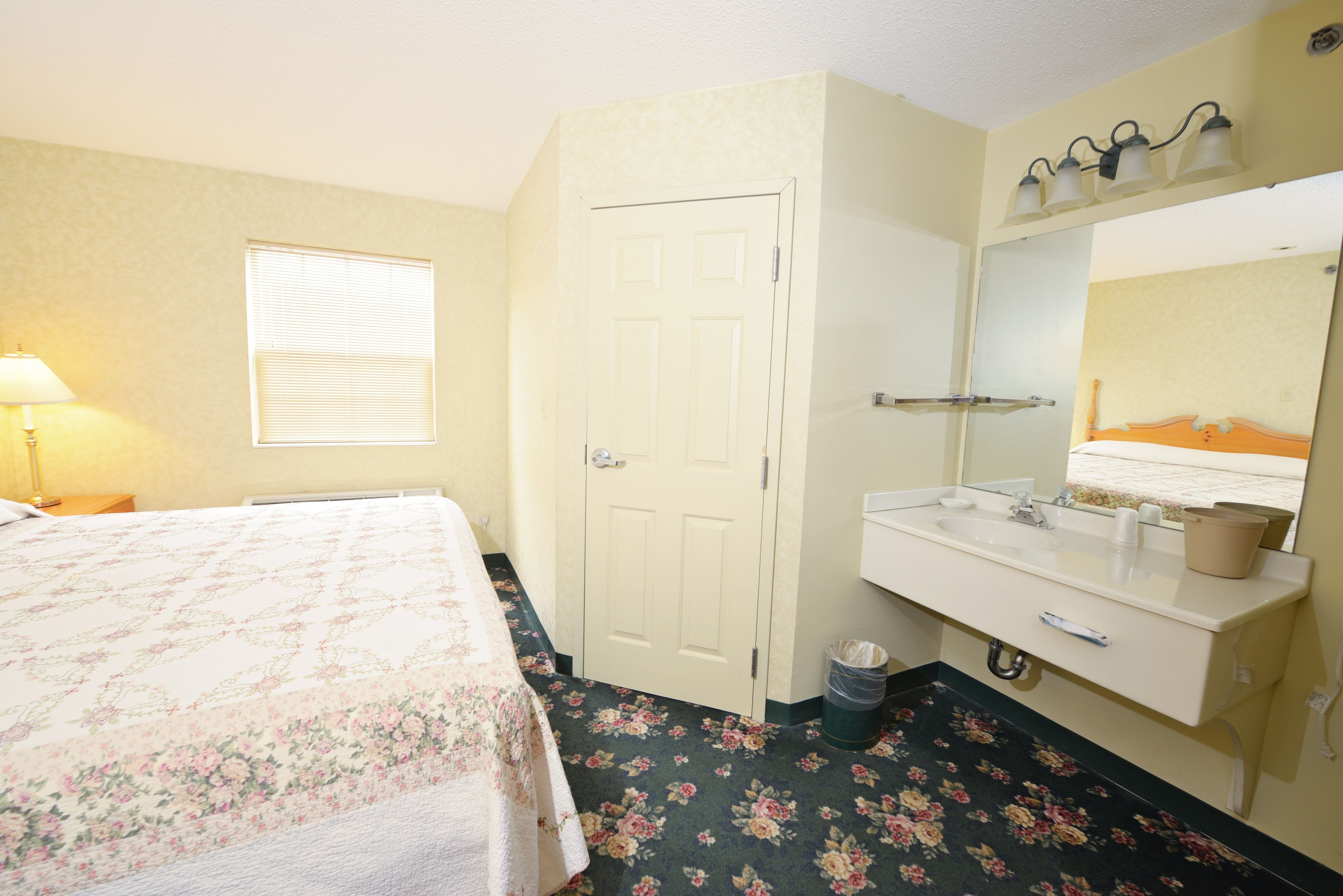 A bedroom with a bed, a window, a door, a sink, and a mirror.