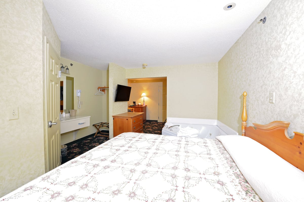 A hotel room with a bed, a wooden dresser, a mirror, a sink, a toilet, and a TV on the wall.