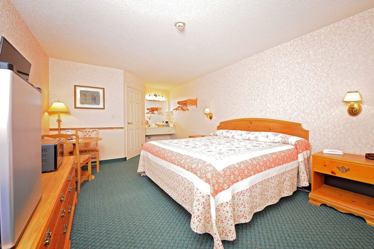 A hotel room with a bed, a desk with a lamp, a dresser, and a television.
