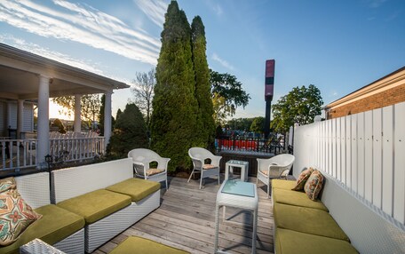 An outdoor patio with wicker furniture, a tall tree, and a brick wall.