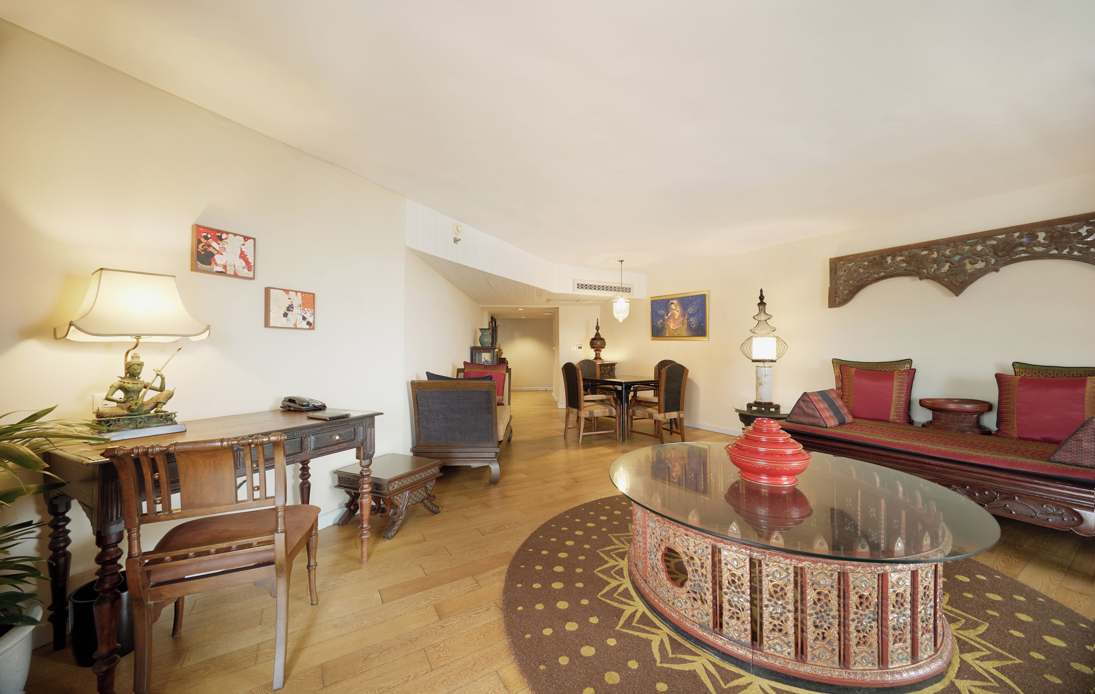 A spacious living room with a round glass coffee table, a sofa, a dining table, and a desk.