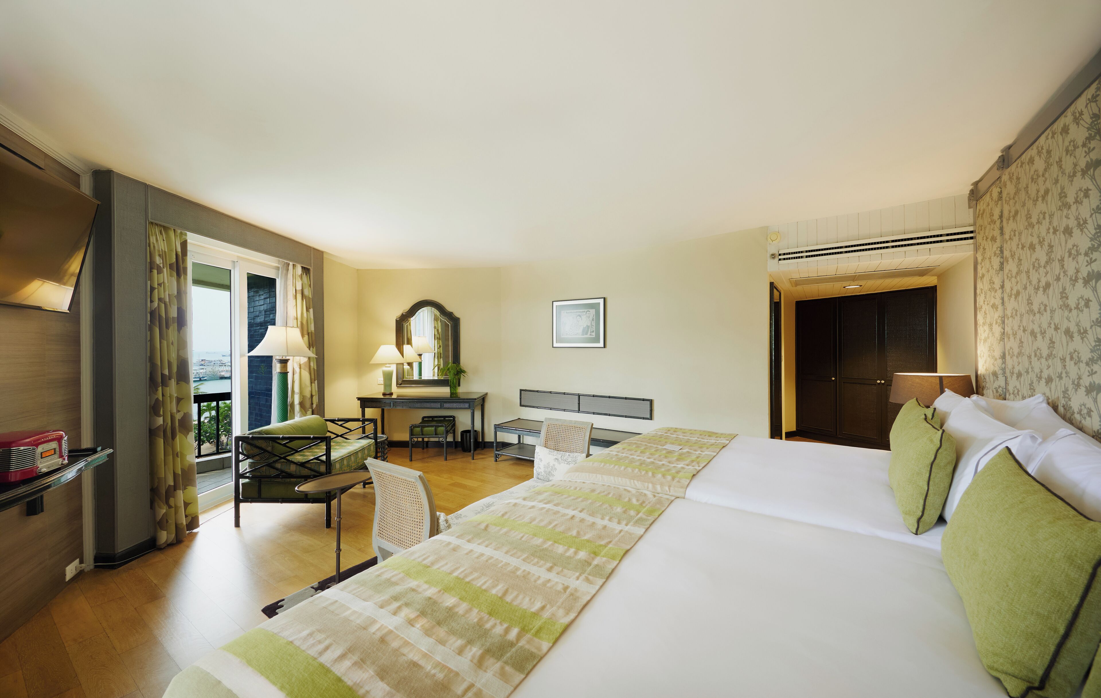 Habitación de hotel con dos camas, un escritorio con silla, un espejo y vistas al exterior.