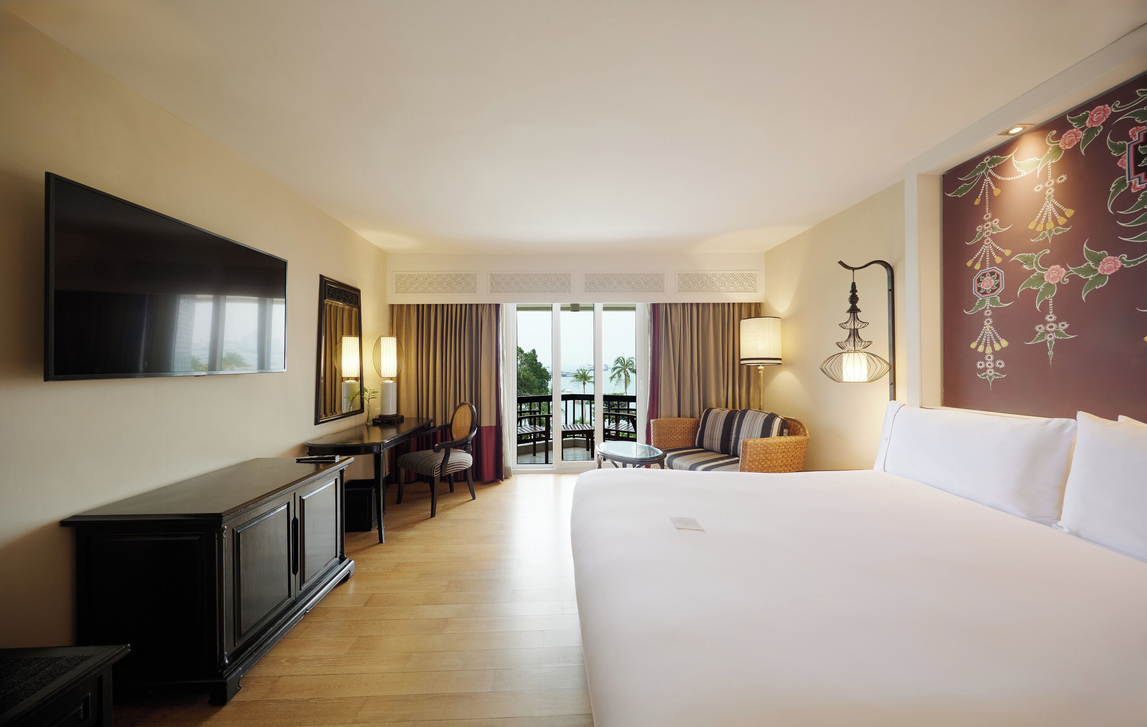 Une chambre d’hôtel dotée d’un grand lit, d’une télévision à écran plat, d’un bureau avec une chaise, d’une petite table et d’un balcon avec des rideaux.