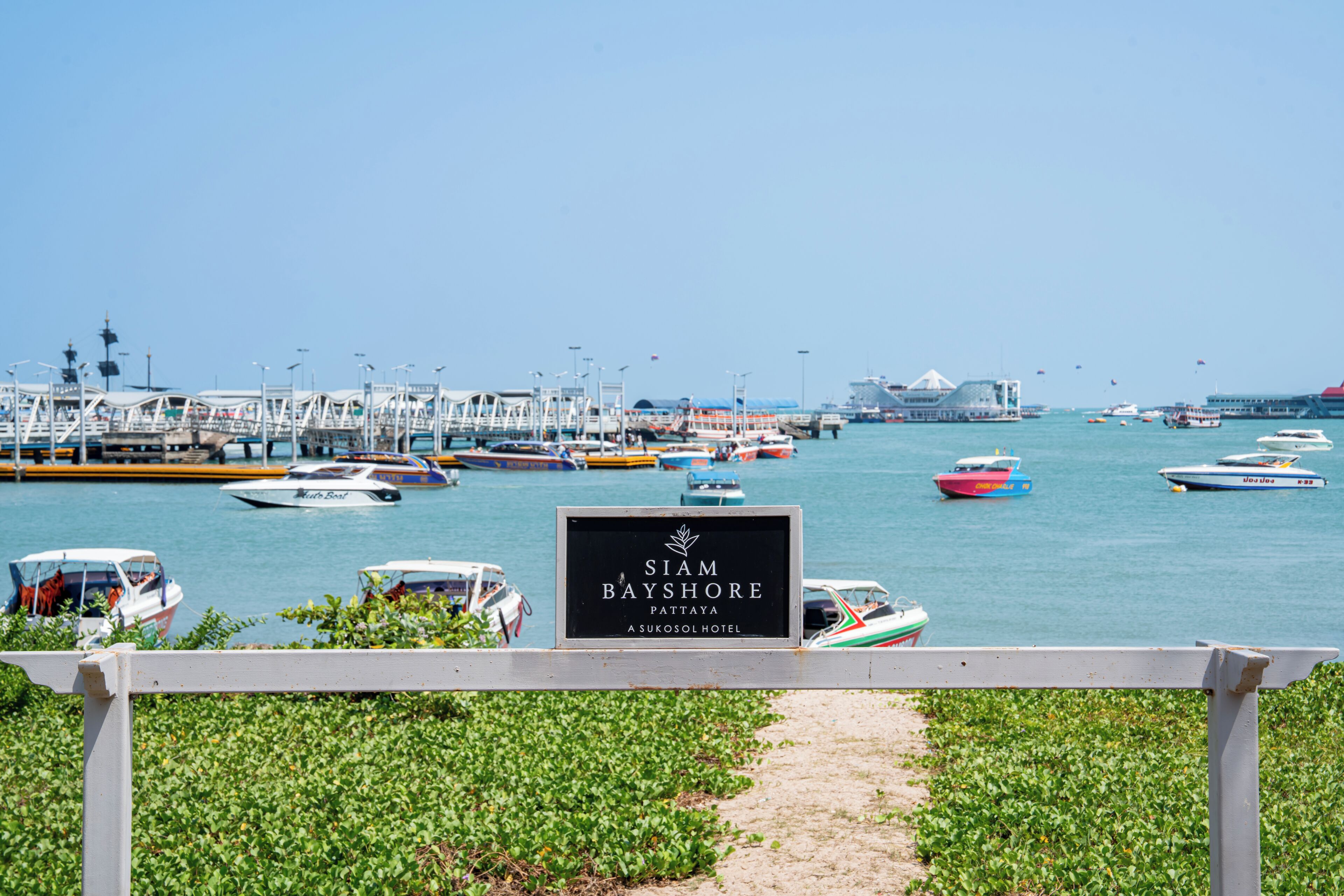 A marina with boats, a sign for Siam Bayshore Pattaya, and a pathway leading to the water.