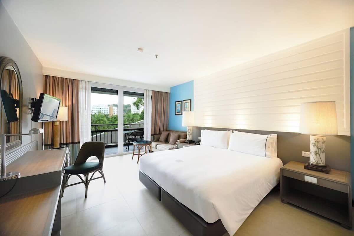 A hotel room with a bed, a desk with a chair, a small table, and a sofa.