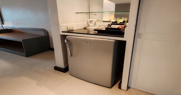 A compact kitchenette with a refrigerator, a coffee maker, and a glass shelf with condiments.