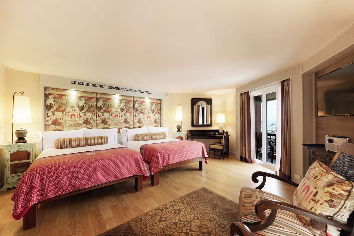 A hotel room with two beds, a desk, a chair, a TV, and a large window with curtains.