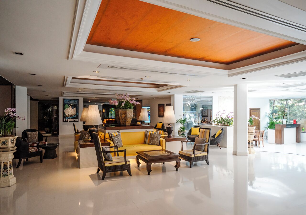 Een ruime lobby met een hoge plafond, een centraal zithoek met banken en fauteuils, en een receptiebalie.