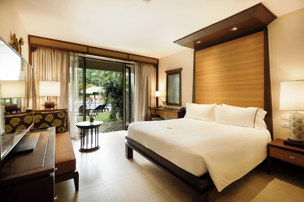 A modern hotel room with a large bed, a desk with a lamp, a chair, and a small table.