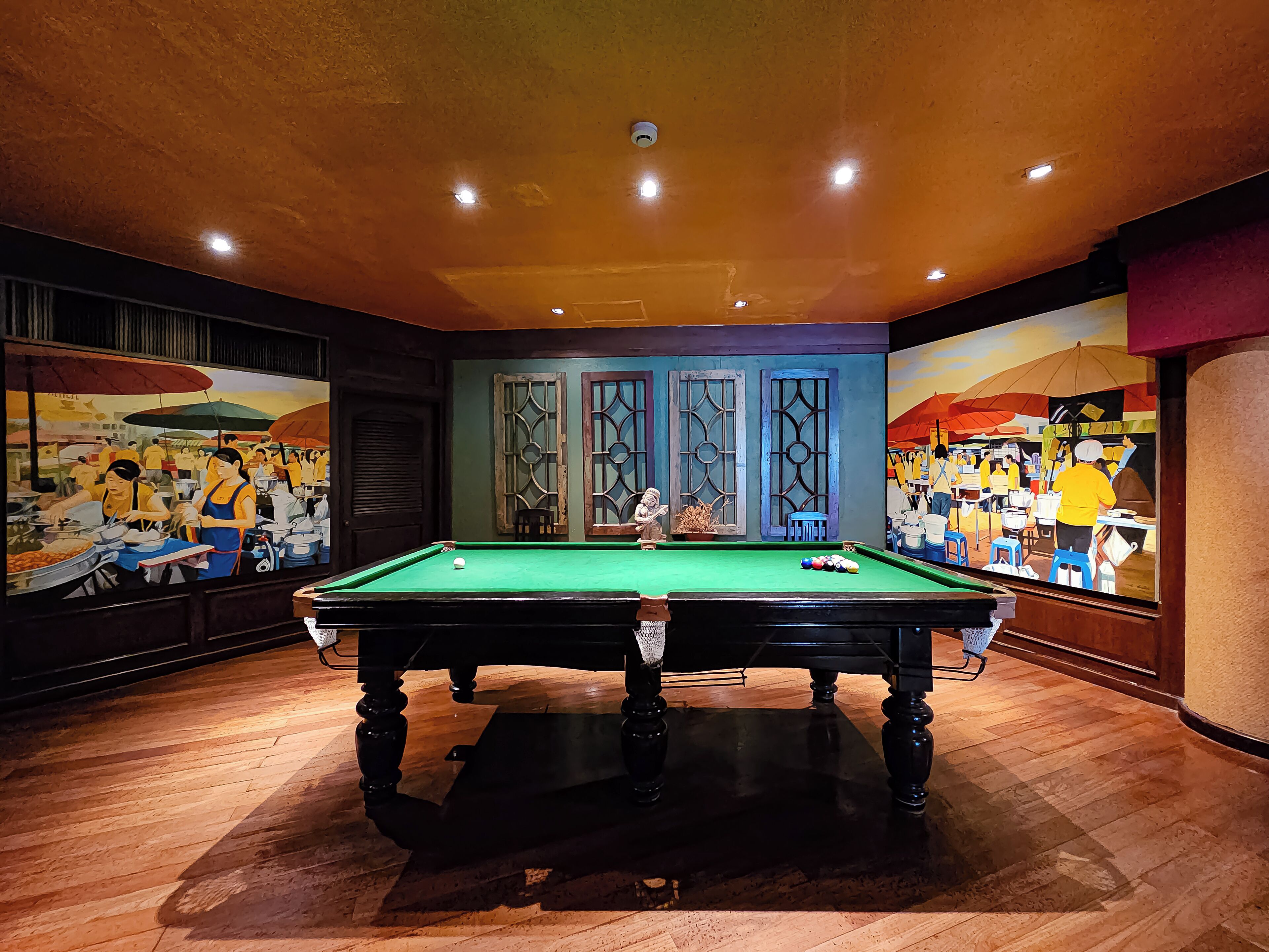 A pool table in a room with wooden flooring and two murals depicting street scenes.