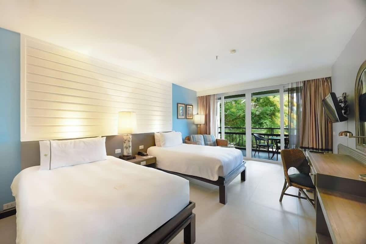 A hotel room with two beds, a desk, a chair, and a balcony with a view.