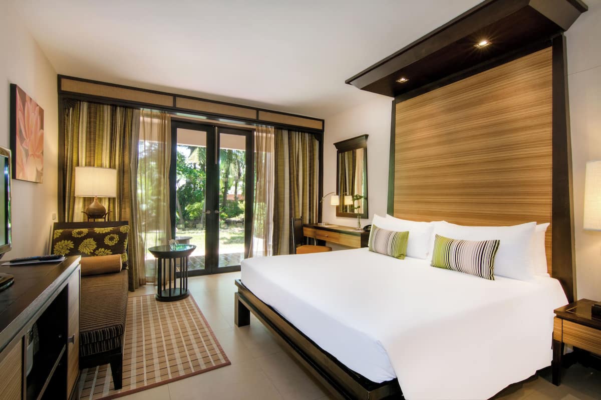 A hotel room with a large bed, a desk, a chair, and a view of the outdoors through a sliding door.